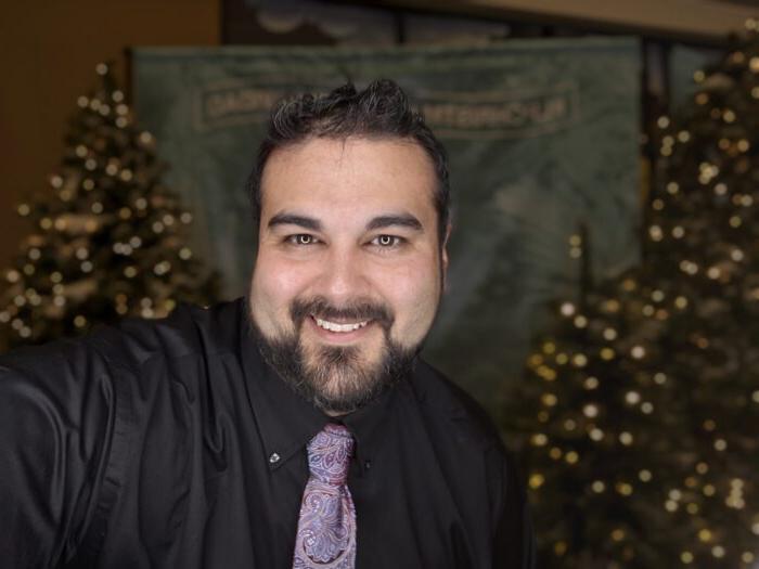 Jeremy Gamez smiling at the camera with Christmas trees behind him.